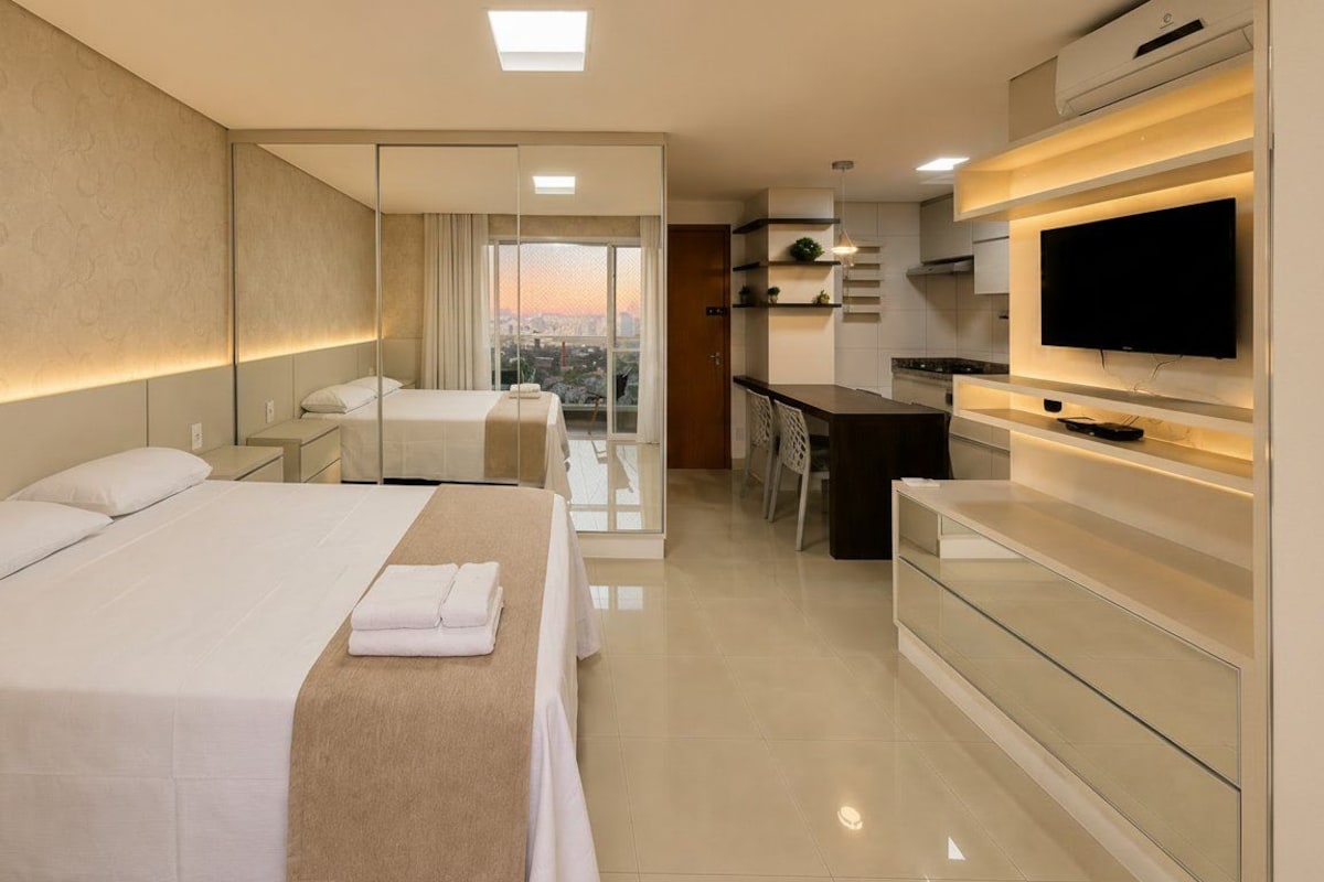 A modern hotel room with a large bed, a TV, a desk, and a balcony with a city view.