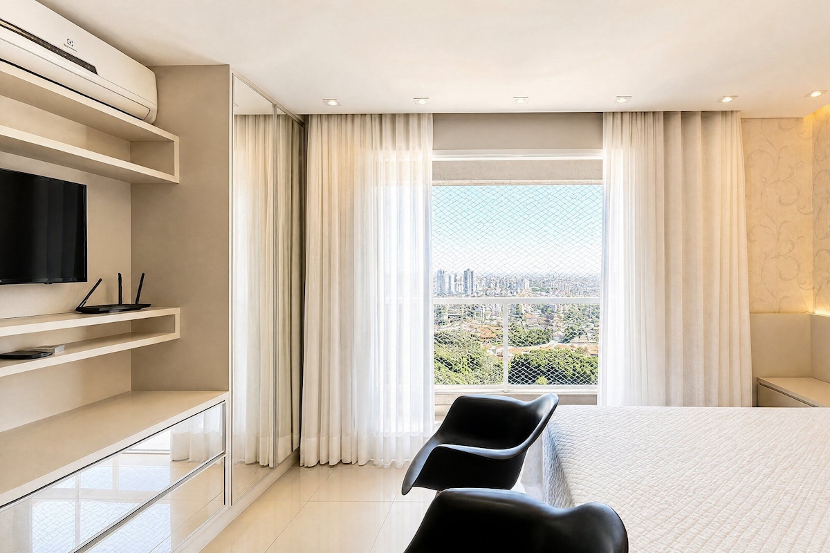 A modern hotel room with a large bed, a TV, and a desk with a computer.