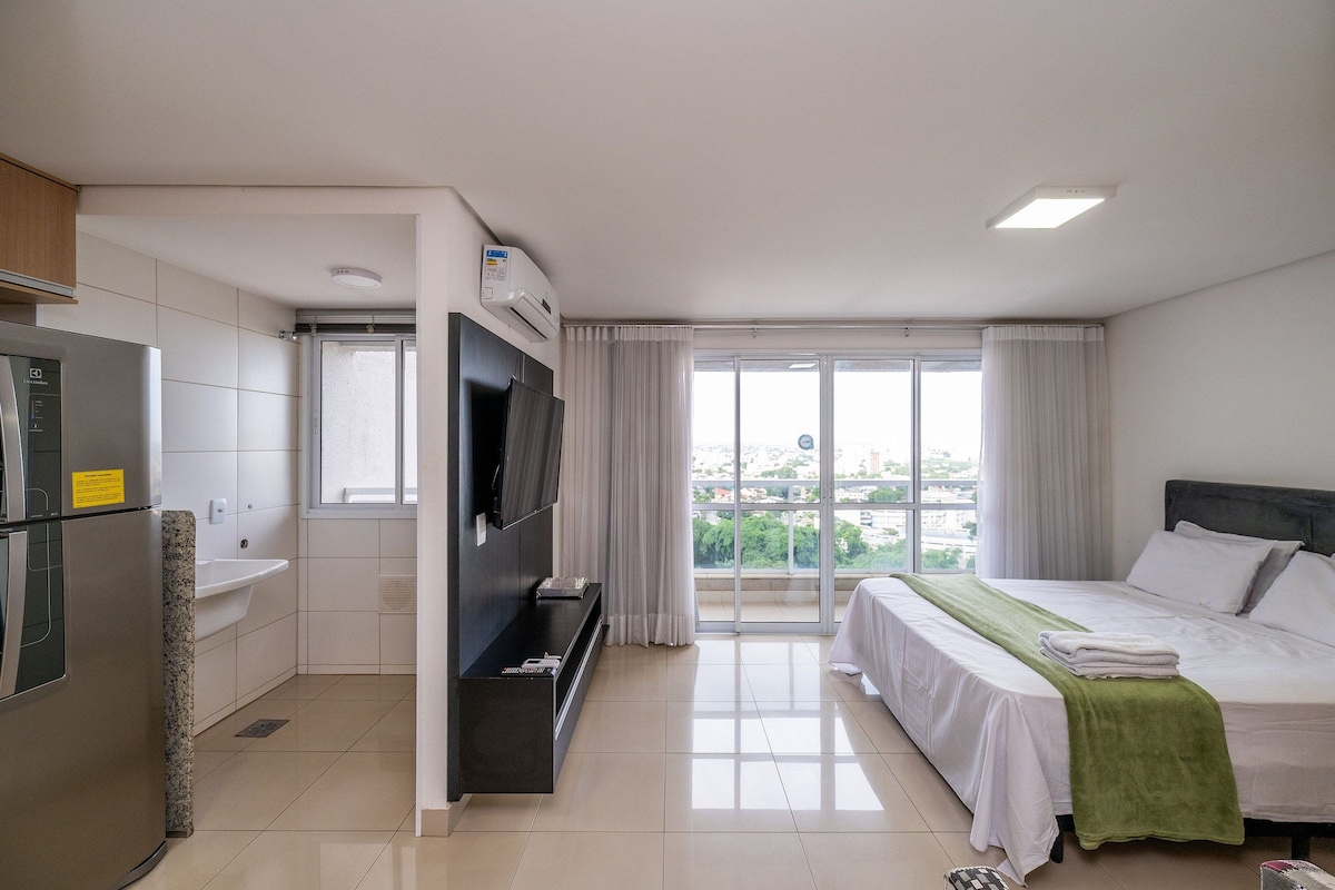 A hotel room with a bed, a TV, a sink, and a window with a view.
