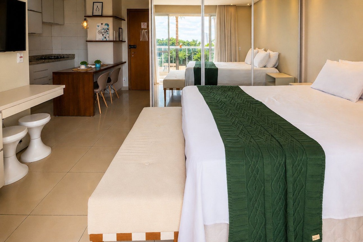 A hotel room with a bed, a bench, a desk, and a balcony with a view.