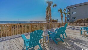 Een houten terras met turquoise Adirondack-stoelen en uitzicht op de oceaan.