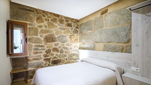 Een slaapkamer met een stenen muur, een houten hoofdbord en een wit sprei.