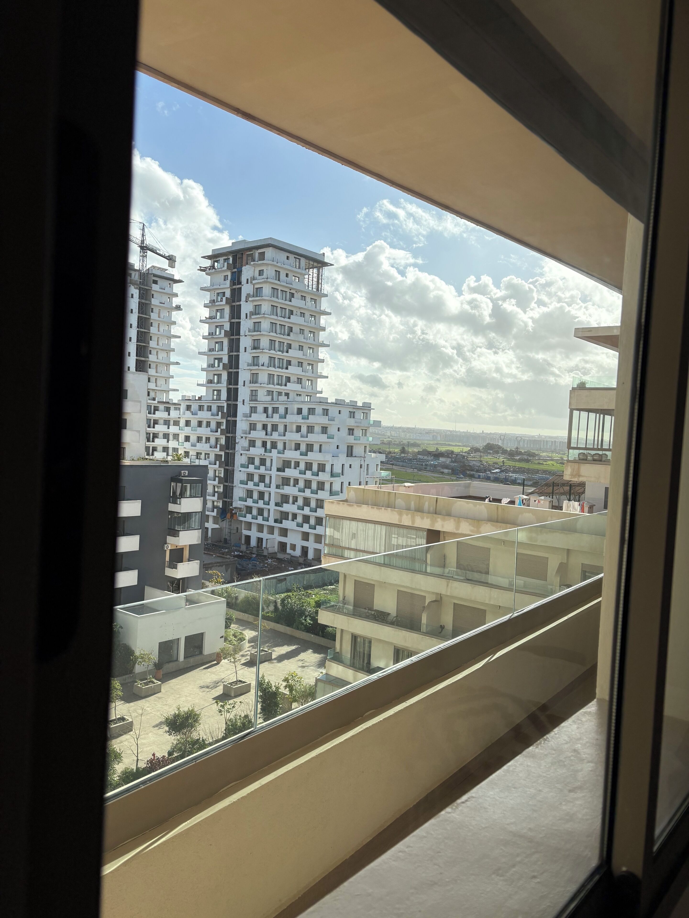 Uitzicht vanaf een balkon op een moderne woonwijk met hoogbouw en een bouwkraan op de achtergrond.