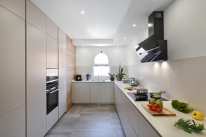 Eine moderne Küche mit weißen Schränken, einem eingebauten Backofen, einem Fenster und einer Arbeitsfläche mit frischem Obst und Gemüse.