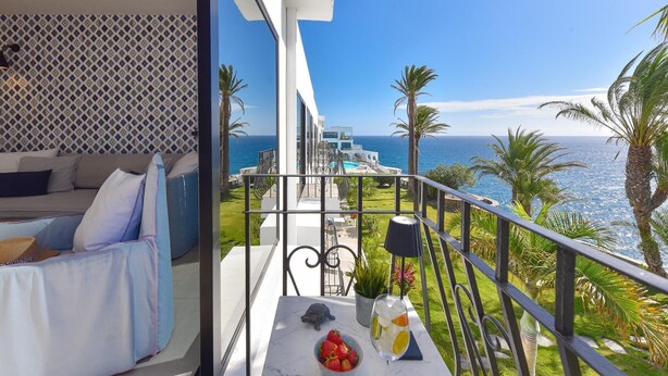 Een balkon met uitzicht op zee, een eettafel met een drankje en een bank.
