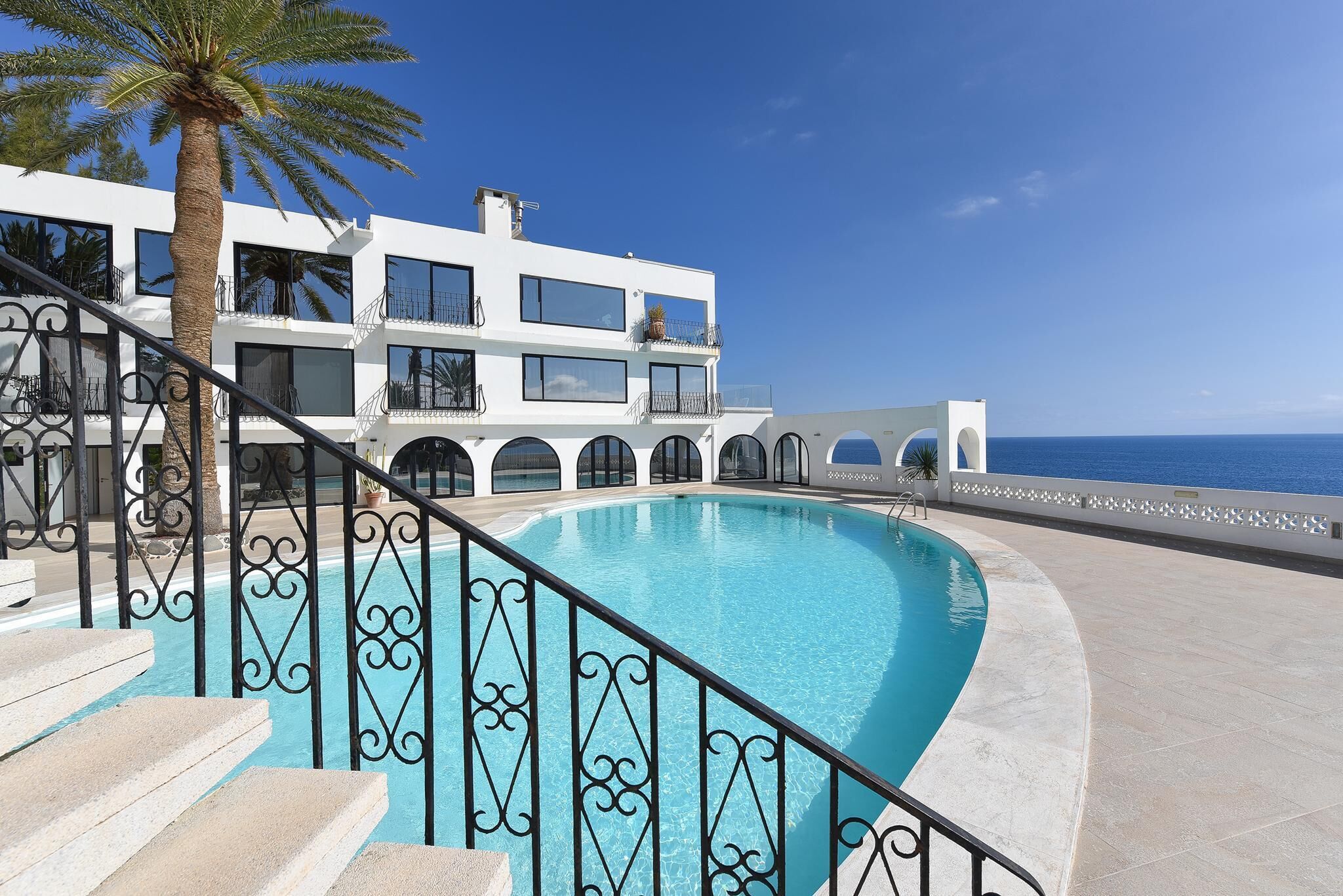 Un edificio moderno con piscina, una escalera con barandillas ornamentales y vistas al mar.