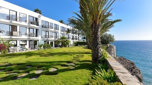 Een modern hotel met meerdere balkons, een verzorgd gazon en uitzicht op zee.