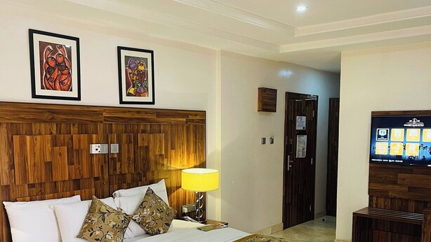 Habitación de hotel con cabecera de madera, cama grande con sábanas blancas, alfombra roja, televisor sobre un soporte de madera y dos obras de arte enmarcadas en la pared.