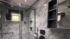 Un baño moderno con ducha de vidrio, un espejo grande y un lavabo blanco.