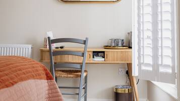 Un dormitorio con cama, escritorio, silla, espejo, radiador, ventana con persianas y cubo de basura.