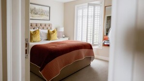 A bedroom with a bed, a nightstand, a lamp, and a window with blinds. - White Hart Netherfield (Battle)