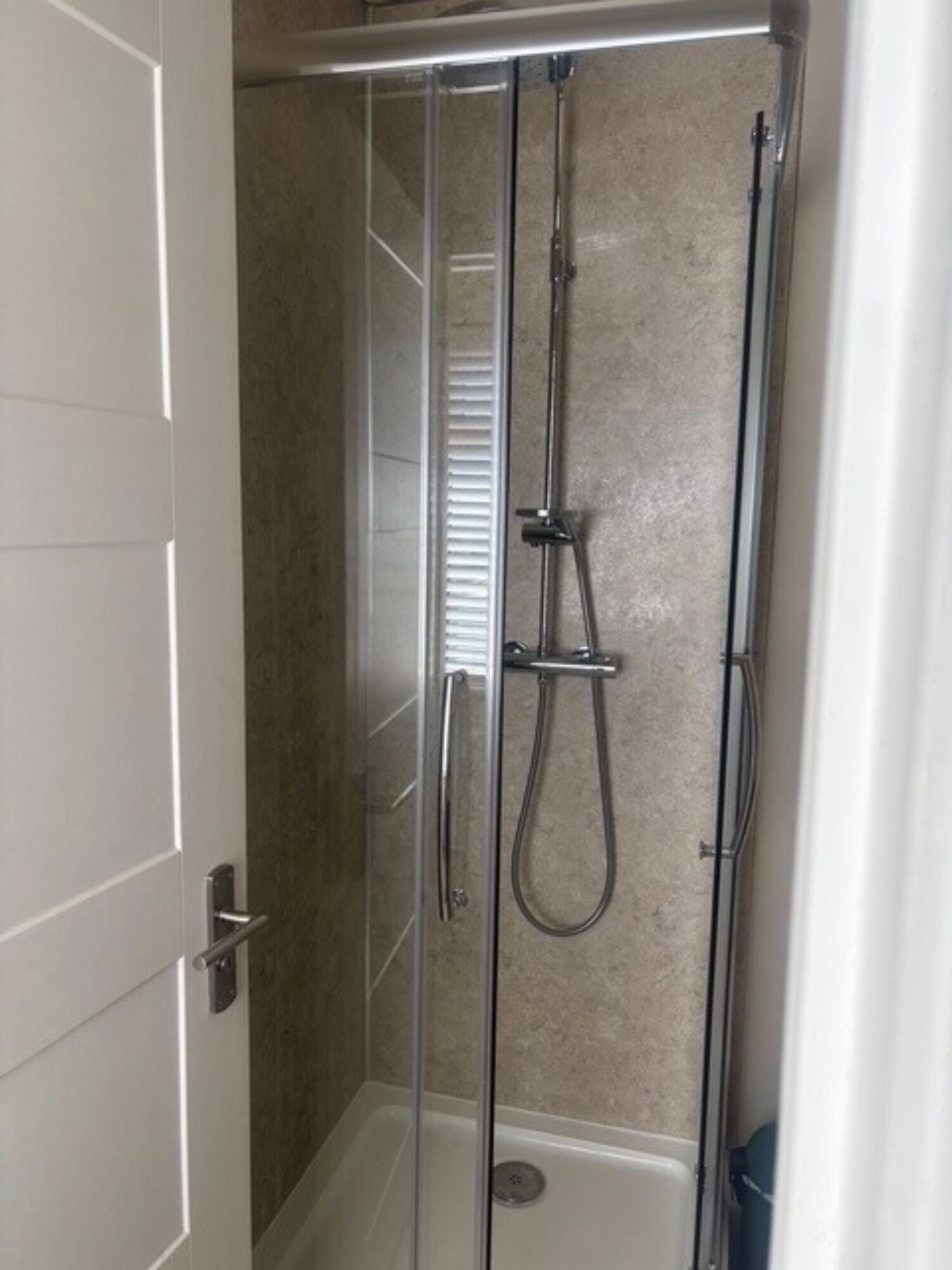 A glass-enclosed shower stall with a handheld showerhead and a wall-mounted faucet.