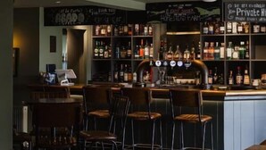 A bar area with stools and a counter, shelves with bottles, and a sign above the bar. - White Hart Netherfield (Battle)