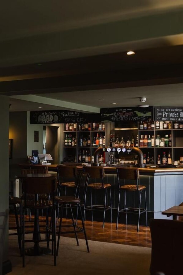 A bar area with stools and a counter, shelves with bottles, and a sign above the bar.