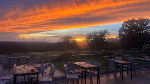 An outdoor seating area with tables and chairs, overlooking a scenic landscape with a sunset. - White Hart Netherfield (Battle)