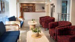 Un vestíbulo de hotel con sofás de diseño azul y rojo, un mostrador de recepción y una pared de madera con estanterías.