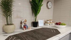 A kitchen counter with potted plants, a framed picture, a clock, and a bowl of fruit.