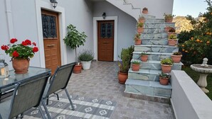 A patio with a glass table and chairs, surrounded by potted plants and a stone staircase.