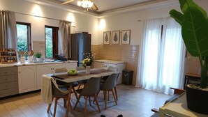 A modern kitchen with a dining table, chairs, a refrigerator, and a potted plant.