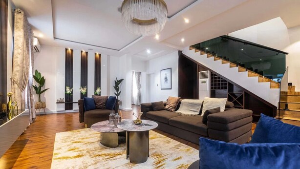 A modern living room with a staircase, a chandelier, and a large window. - Muftyz Shortlets (Abuja)