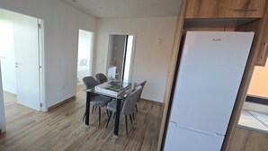 Eine moderne Küche mit einem weißen Kühlschrank, Holzschränken und einem Essbereich mit einem Glastisch und Stühlen.