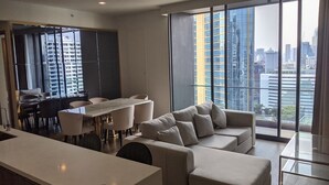 Un soggiorno moderno con un divano, un tavolo da pranzo e sedie. Una grande finestra offre vista sulla città.