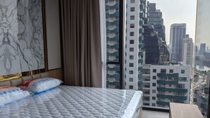 Une chambre avec un grand lit, une vue sur de hauts immeubles et un banc en bois.