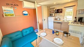 Una cocina compacta con microondas, estufa y pileta. Se ve también un sofá azul y una pequeña mesa de comedor con platos y un hervidor.