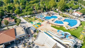 Luchtbeeld van een resort met meerdere zwembaden, een waterglijbaan en een verzorgd gazon.