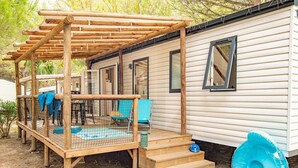 Een stacaravan met een houten terras, een overdekte zithoek en een kleine buitenkeuken.