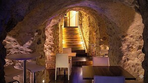 Un restaurant souterrain aux murs de pierre, avec un escalier menant à un niveau supérieur et un aménagement moderne des espaces de repos.