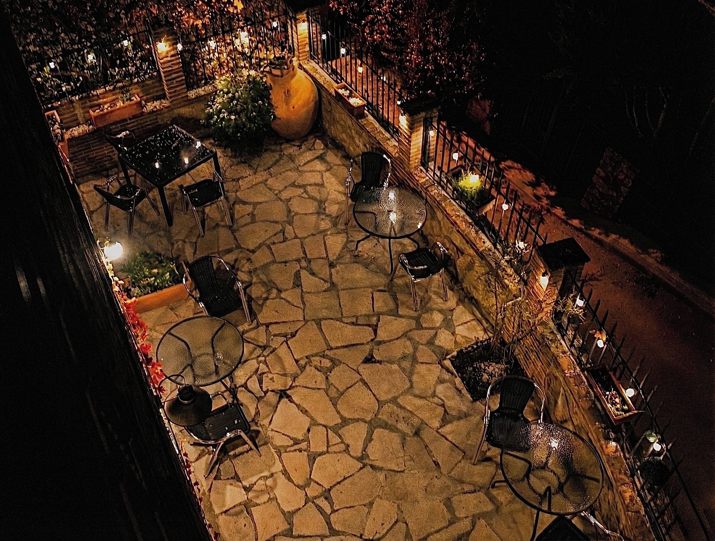 An outdoor patio area with stone flooring, multiple tables and chairs, and a railing along the perimeter.
