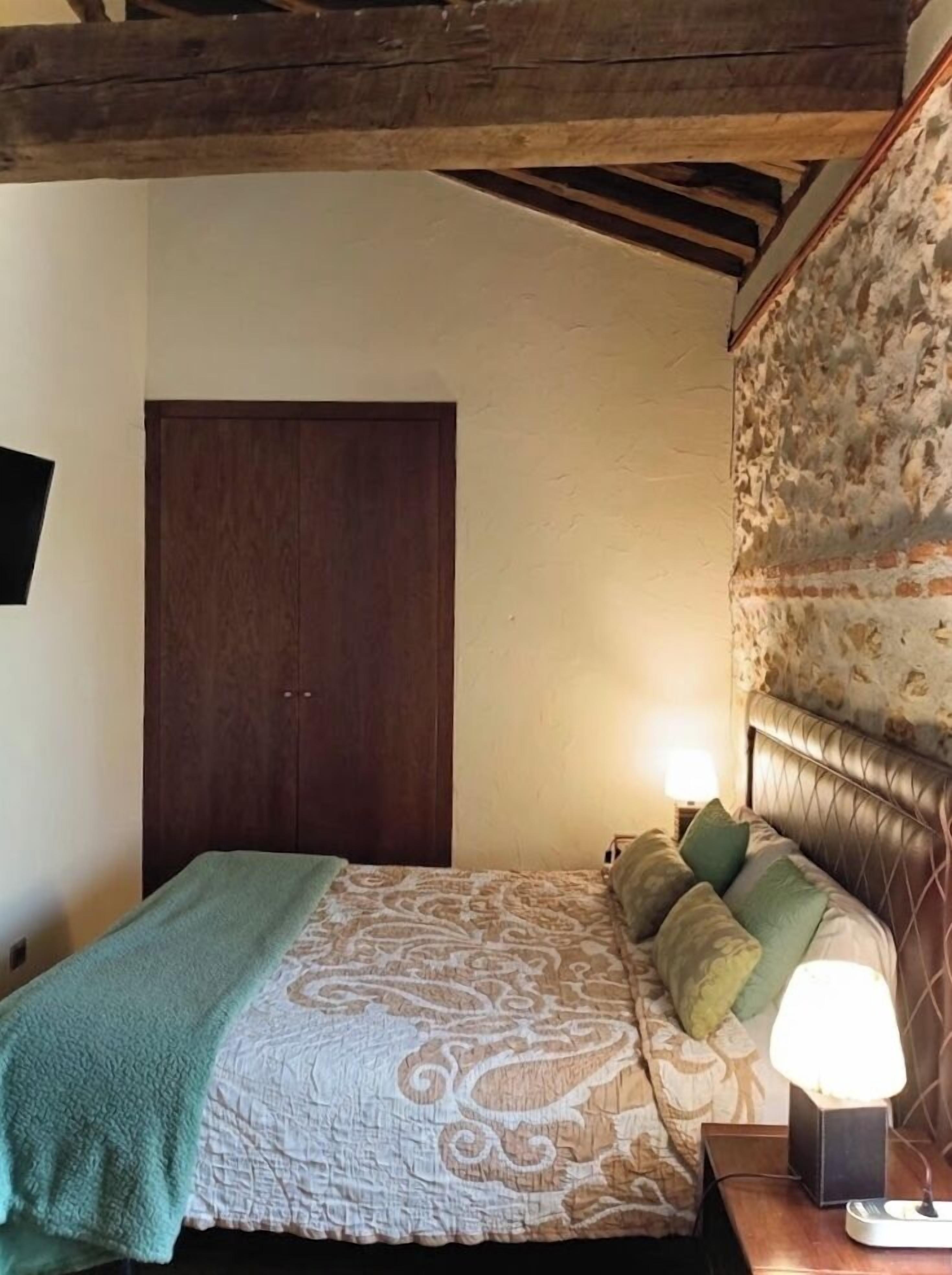 A bedroom with a bed, a nightstand, a lamp, and a wooden ceiling.