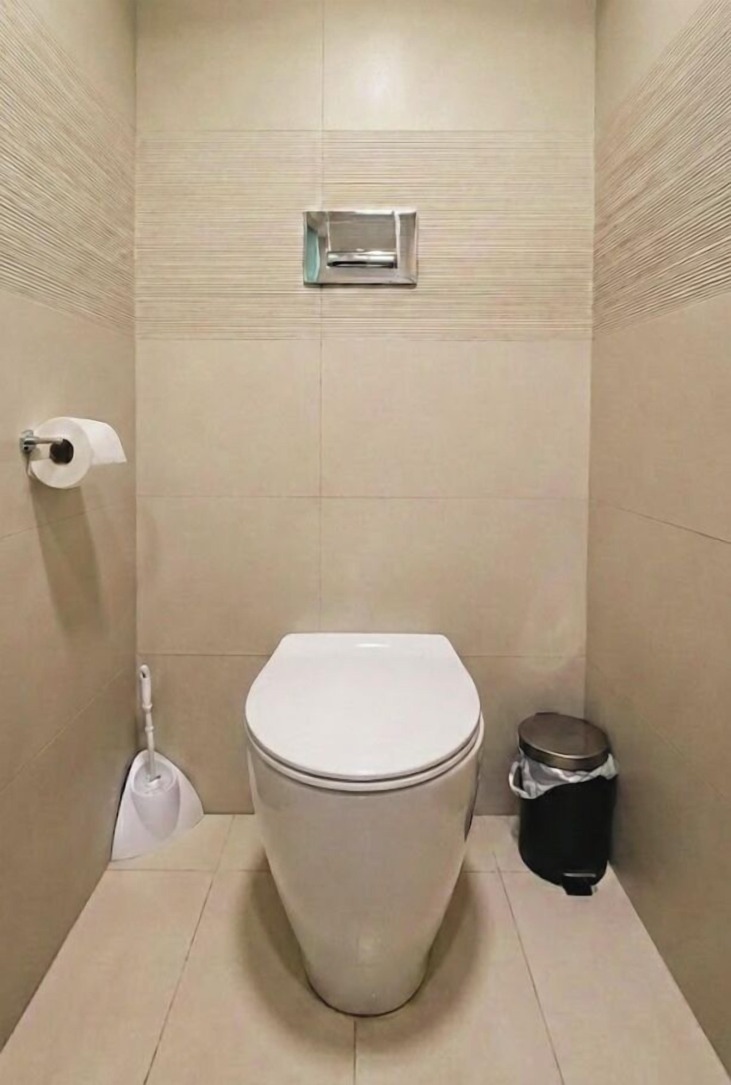 A small, enclosed bathroom with a toilet, a trash bin, and a toilet paper holder on the wall.