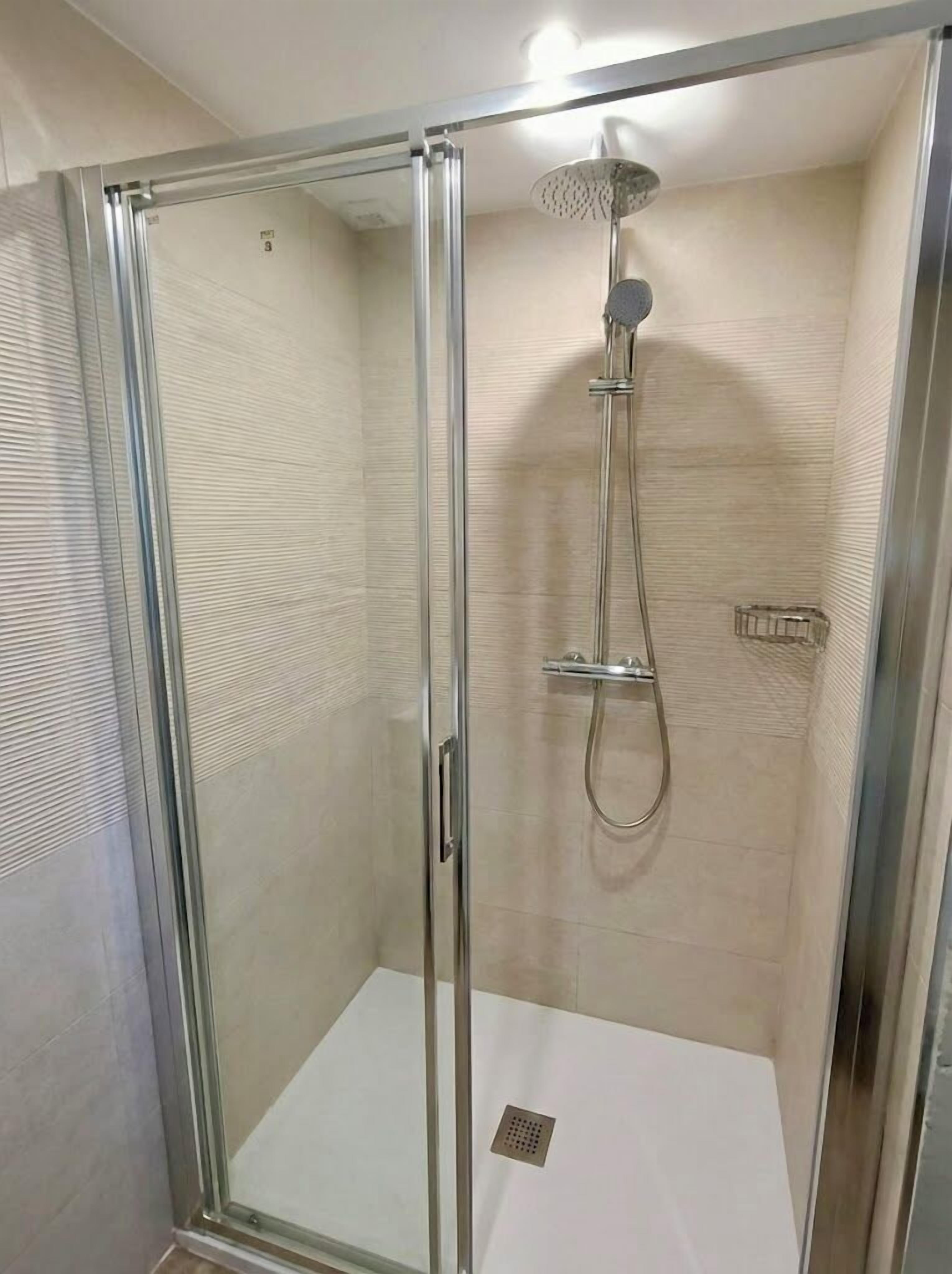 Eine Duschkabine mit Handbrause und am Wand montiertem Wasserhahn.