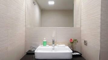 Une salle de bain avec un lavabo blanc, un miroir au-dessus et un petit vase avec une fleur posé sur le comptoir.