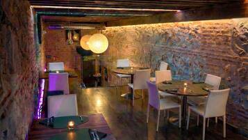 A restaurant with a rustic stone wall, wooden tables, and modern lighting.