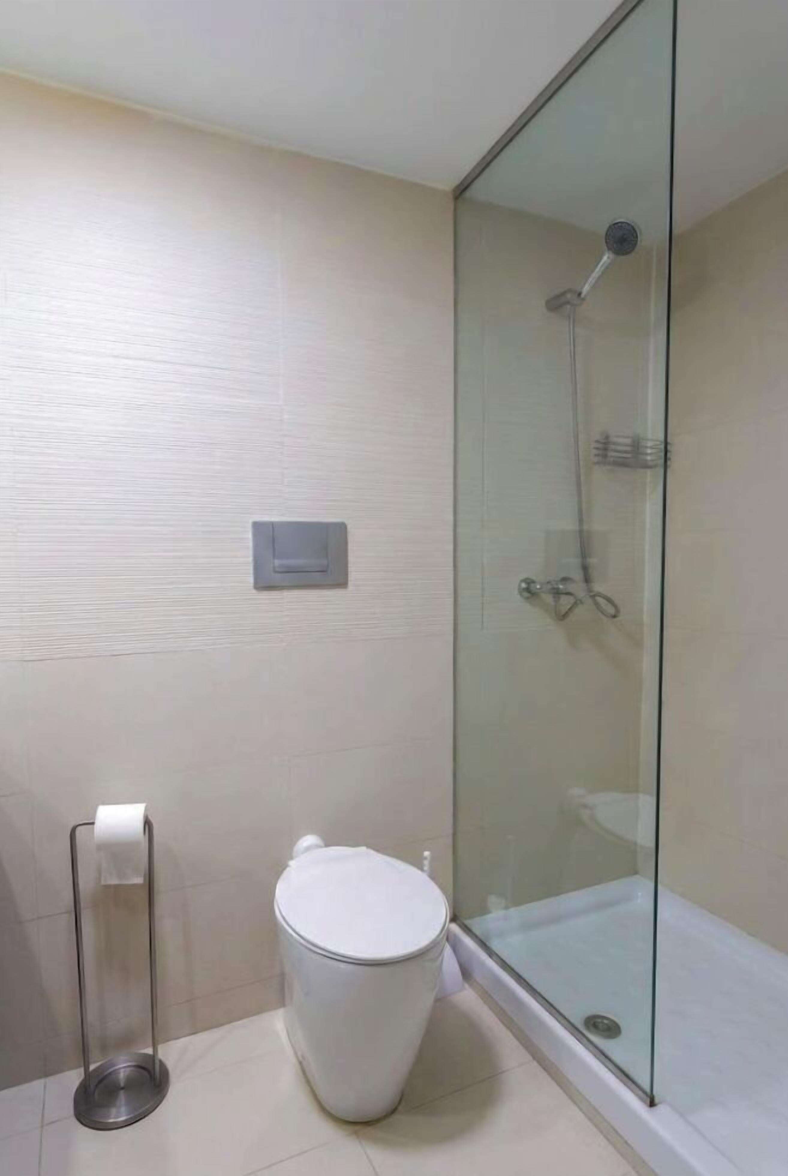 A bathroom with a glass-enclosed shower, a toilet, and a paper towel holder.