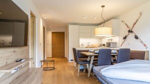 Una habitación de hotel moderna con piso de madera, una cama, un escritorio con sillas, una zona de cocina y esquíes colgados en la pared.
