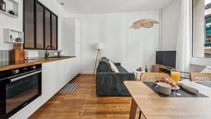 Una cocina moderna con horno empotrado, un área de comedor con mesa lista para el desayuno, y un sofá en la sala.