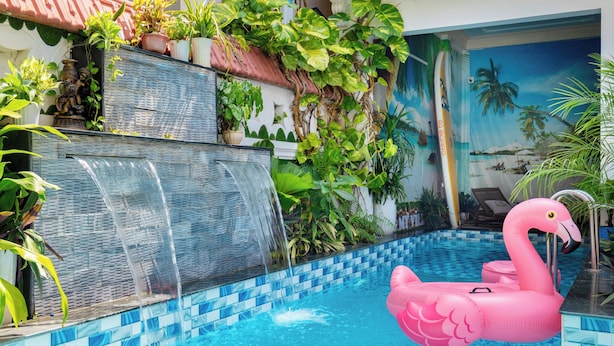 Una piscina con un flotador con forma de flamenco rosa, una cascada y abundante vegetación alrededor del área de la piscina.