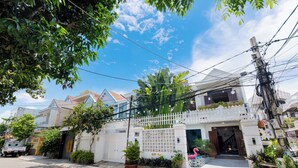 Una casa residencial con fachada blanca, entrada protegida por un portón y un pequeño jardín con plantas en macetas.