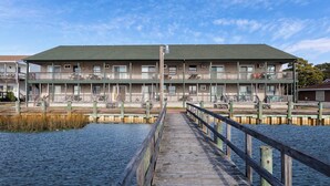 Ein Motel am Wasser mit einer Holzterrasse, die zum Gebäude führt, mit mehreren Balkonen und einer flachen Dachfläche.