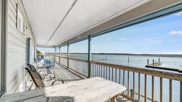 Eine überdachte Terrasse mit Blick auf das Wasser, Holzstühle und ein Tisch.