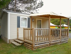Ein kleines, eingeschossiges Mobilheim mit einer Holzterrasse und einer überdachten Veranda.