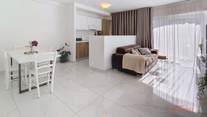 Een moderne woonkamer met een eethoek, een keuken en een groot raam met gordijnen.