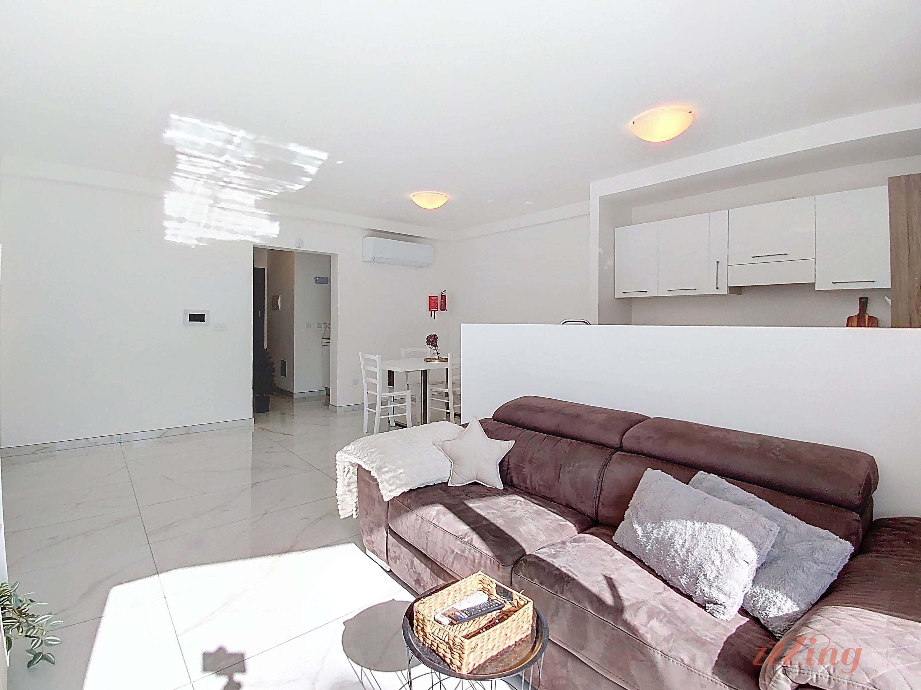 A modern living room with a brown sofa, a small round table, and a dining area in the background.