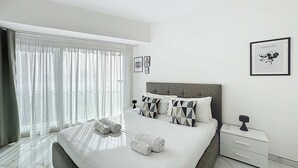 Een moderne slaapkamer met een groot bed, een nachtkastje, een ingelijste foto aan de muur en een raam met dunne gordijnen.
