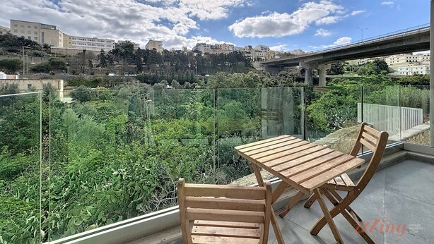 Een balkon met een houten tafel en stoelen, met uitzicht op een stadsgezicht met gebouwen en groen.