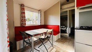 Eine kompakte Küche mit Essbereich, einer roten Bank und einem Fenster mit Vorhängen.